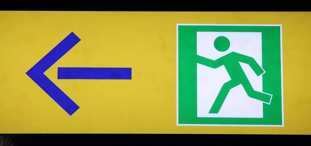 Señal de salida de emergencia con una flecha apuntando hacia la izquierda, ilustrando de forma visual el concepto de por qué huyo cuando alguien me gusta y la tendencia a escapar ante la cercanía emocional