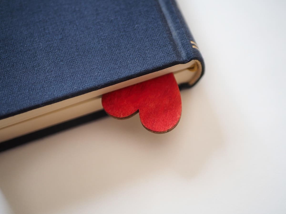 Marcapáginas con forma de corazón rojo sobresaliendo de un libro, representando el proceso de duelo amoroso en vacaciones y la sanación emocional