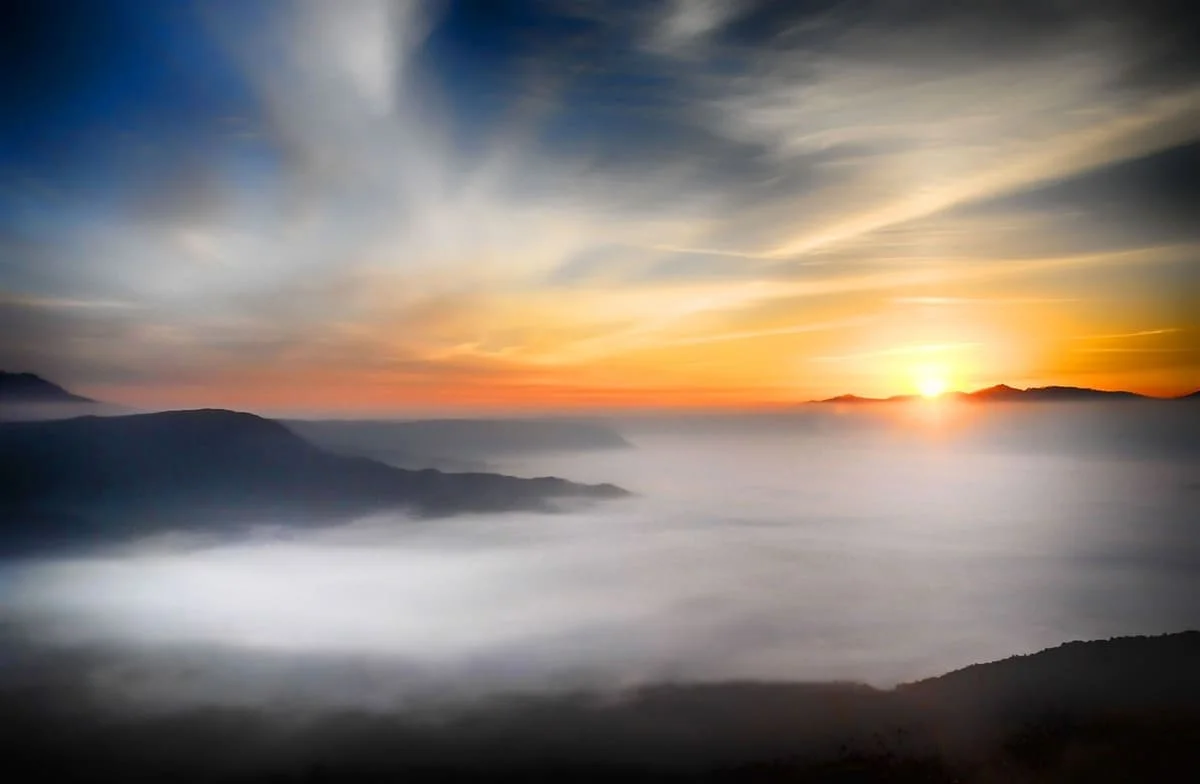 Como afecta el sol a las emociones con imagen del sol sobre montañas nubladas